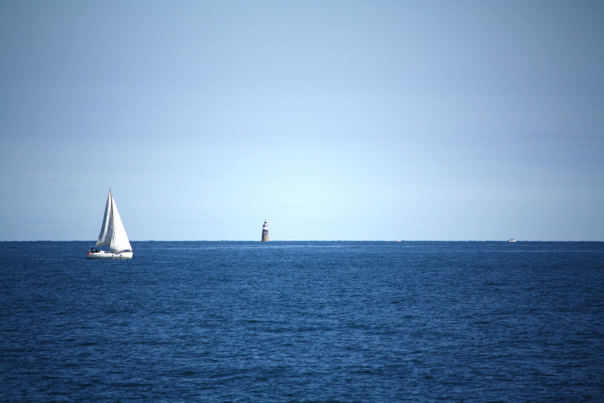 Un voilier passe devant un phare en pleine mer